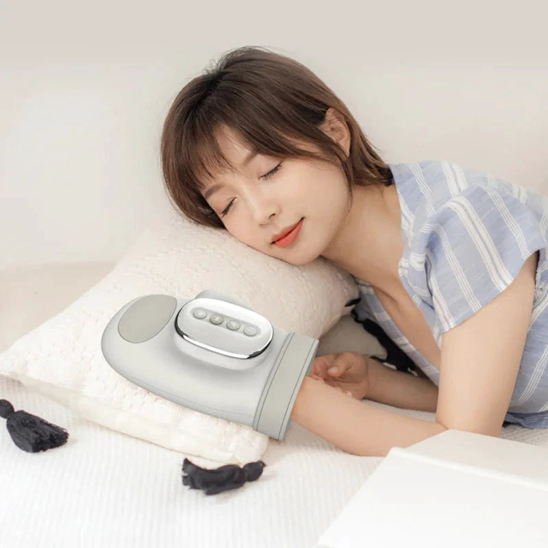 Sleeping woman on a pillow with a silver wireless hand-and-wrist massager on her forearm, featuring a rounded control panel with four buttons.